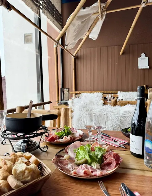 Interior of the restaurant 'Le K2', with a mountain or Nordic lodge theme, featuring wooden furniture, white furs, and a antler chandelier