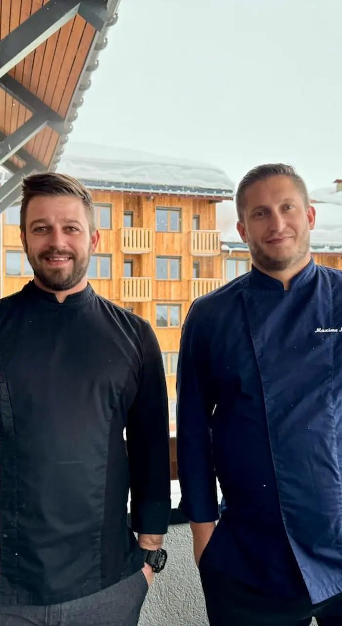 Overhead view of a wooden table set for a fondue and raclette, with charcuterie, bread, salad, and wine.