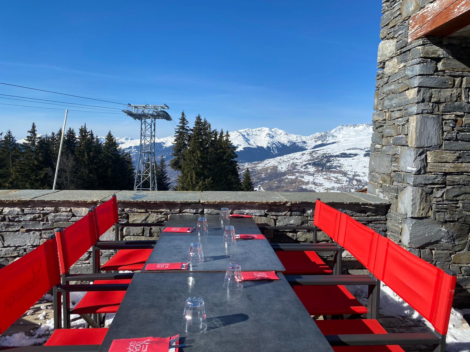 Gros plan sur l'enseigne 'VÔGA GOGA' en grandes lettres blanches modernes avec un logo de bois de cerf stylisé, fixée sur un mur extérieur de pierres grises. La porte d'entrée en bois et verre, affichant les mots 'PUB' et 'RESTAURANT', est visible à droite