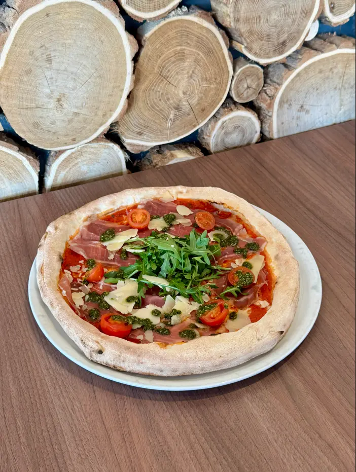 Extérieur d'un bâtiment de type chalet de montagne, avec un mur en pierre et une terrasse en bois, affichant une grande enseigne 'VOGA GOGA' avec un logo de bois de cerf. Une chaise de réalisateur rouge portant le même logo est visible au premier plan, sous un ciel bleu nuageux