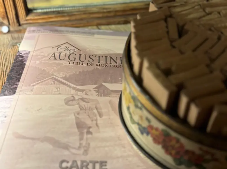 Menu vintage de la brasserie Les Augustins à côté d'une boîte en métal ancienne remplie de dominos en bois.