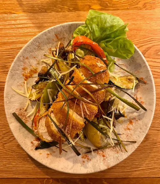 Intérieur du restaurant Chaudron Magique, mettant en valeur une ambiance chaleureuse et rustique de chalet. Le décor présente des poutres et des boiseries brutes foncées, avec des tables en bois dressées. Les chaises sont recouvertes d'épaisses peaux ou fourrures blanches pour un confort montagnard. L'éclairage est tamisé et accentue l'atmosphère intime.