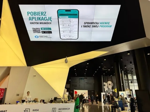 Lobby with people and a large digital screen advertising to download the Freedom Games app and check the agenda to create a personal program.