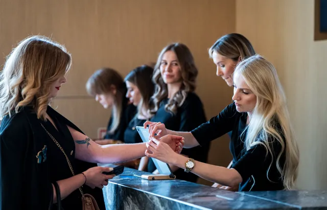 Pięć kobiet interagujących przy recepcji lub stanowisku obsługi klienta, dwie z nich korzystają z tabletu na marmurowym blacie.