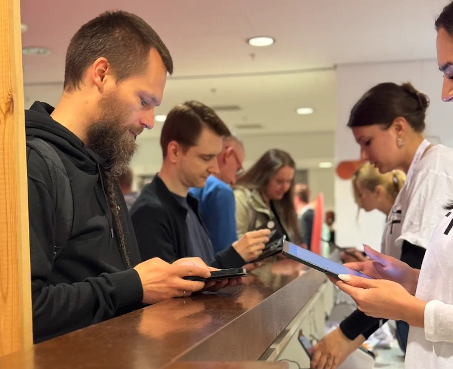 Grupa ludzi stojących przy ladzie, skupionych na tabletach i smartfonach.