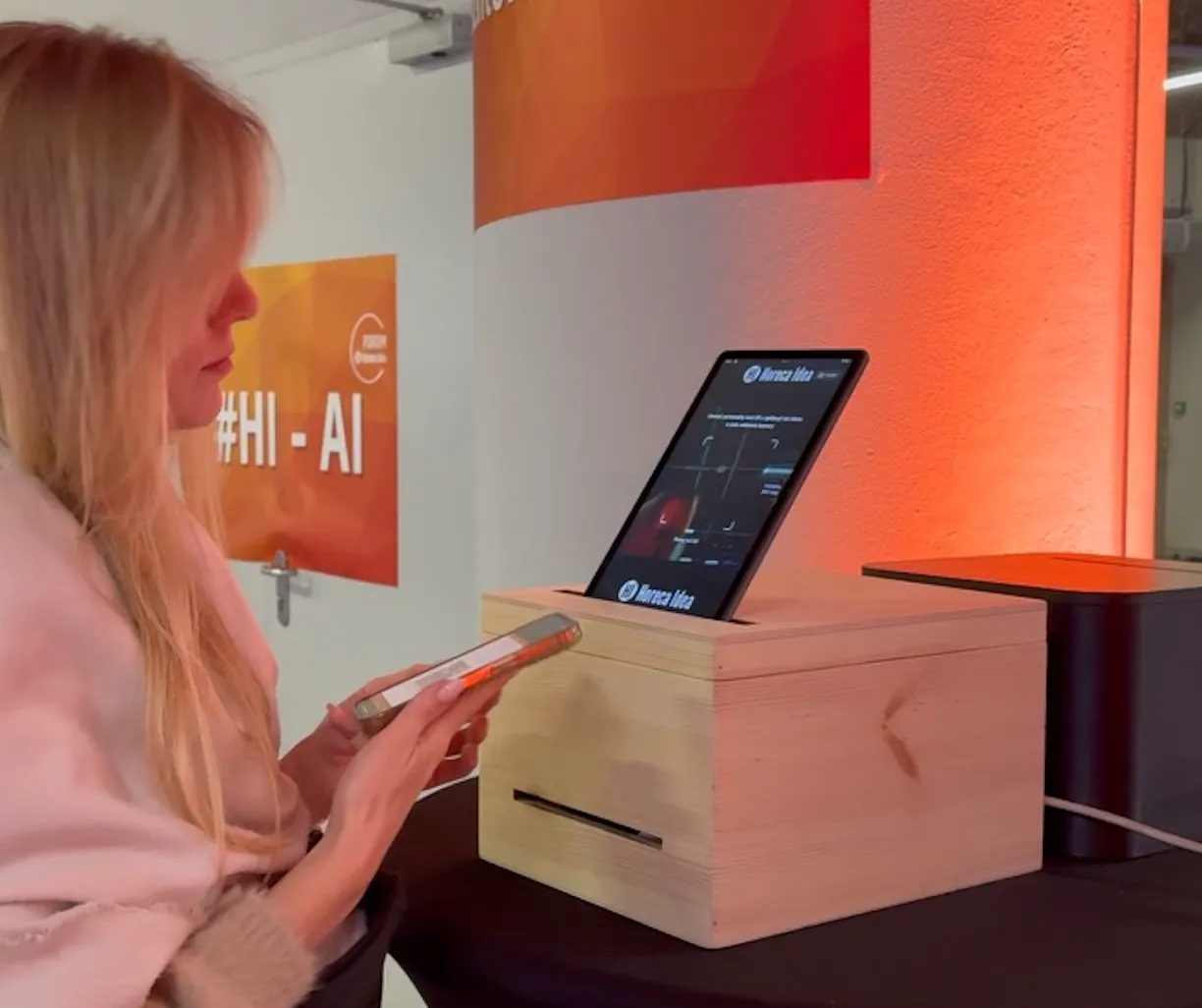 Kobieta trzyma smartfon i korzysta z urządzenia do skanowania twarzy z ekranem na drewnianym stojaku.