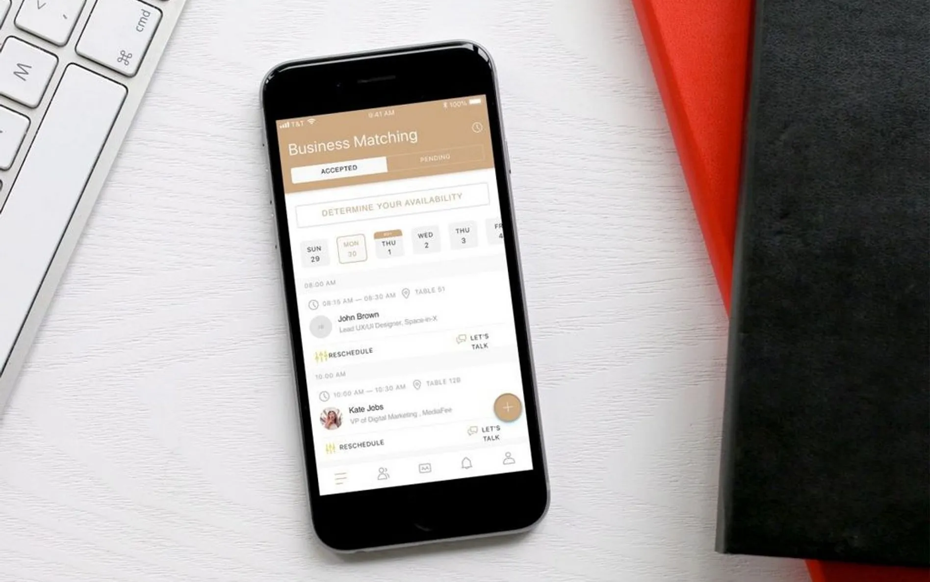 Smartfon na białym biurku obok klawiatury, z ekranem pokazującym aplikację Business Matching z listą spotkań i kalendarzem dostępności.