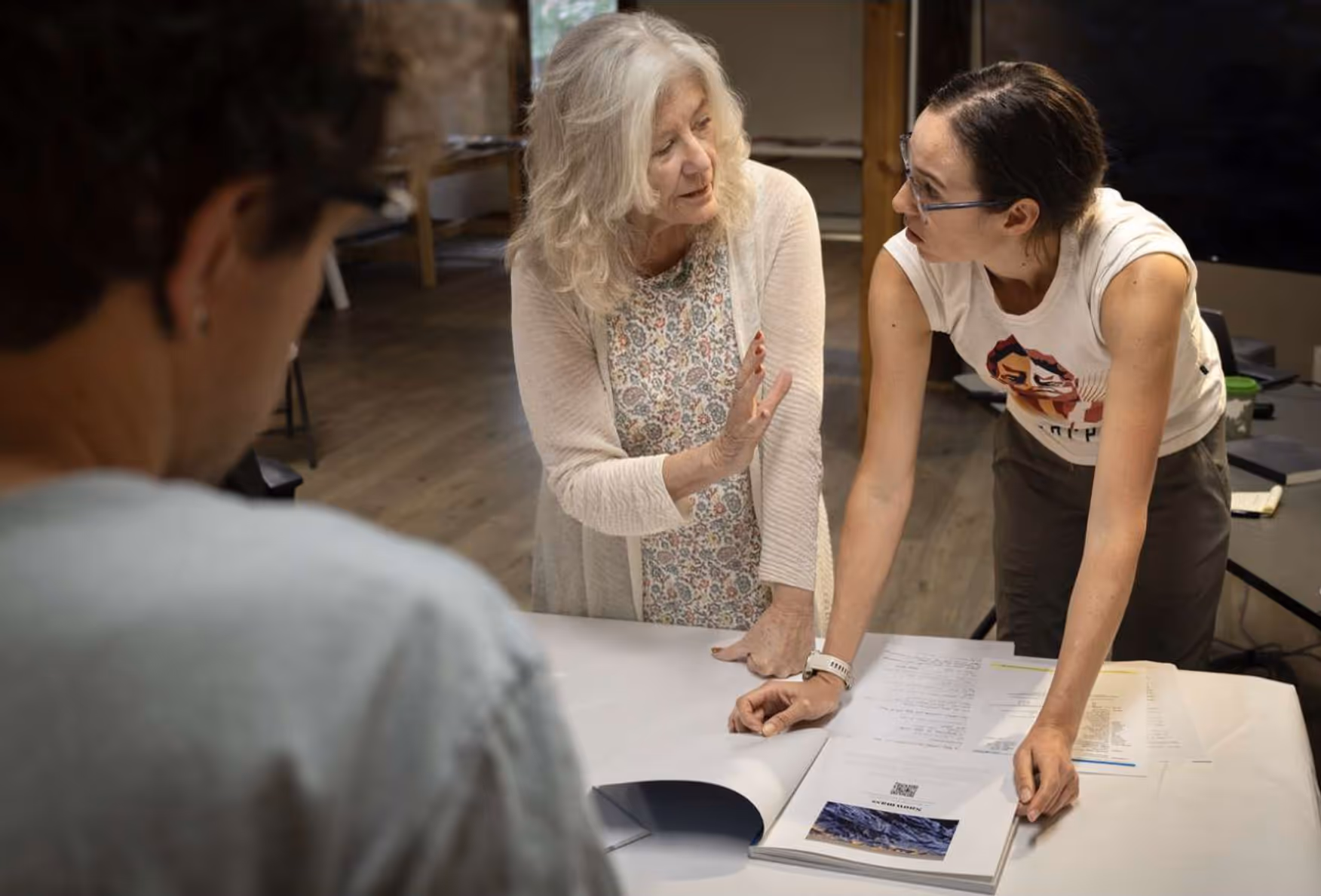 Three people discussing documents on a table in an indoor workspace.
