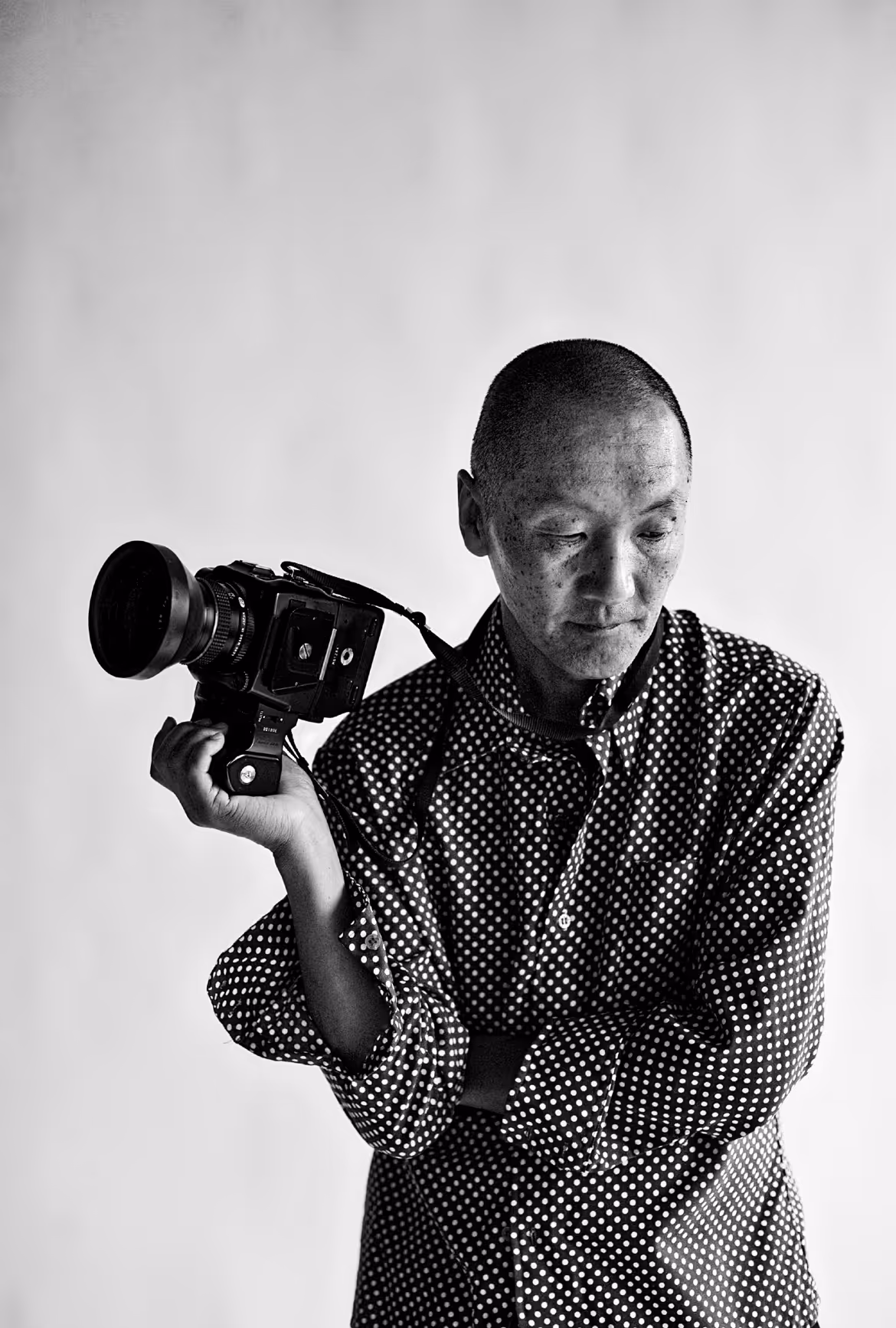 Black and white portrait of a man in a polka dot shirt holding a large camera on his shoulder.