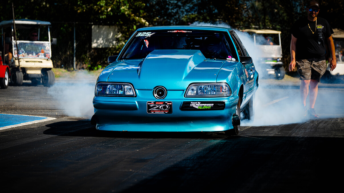 Blue sports car performing a burnout on a racetrack with smoke around the rear tires with Streetcar Addiction