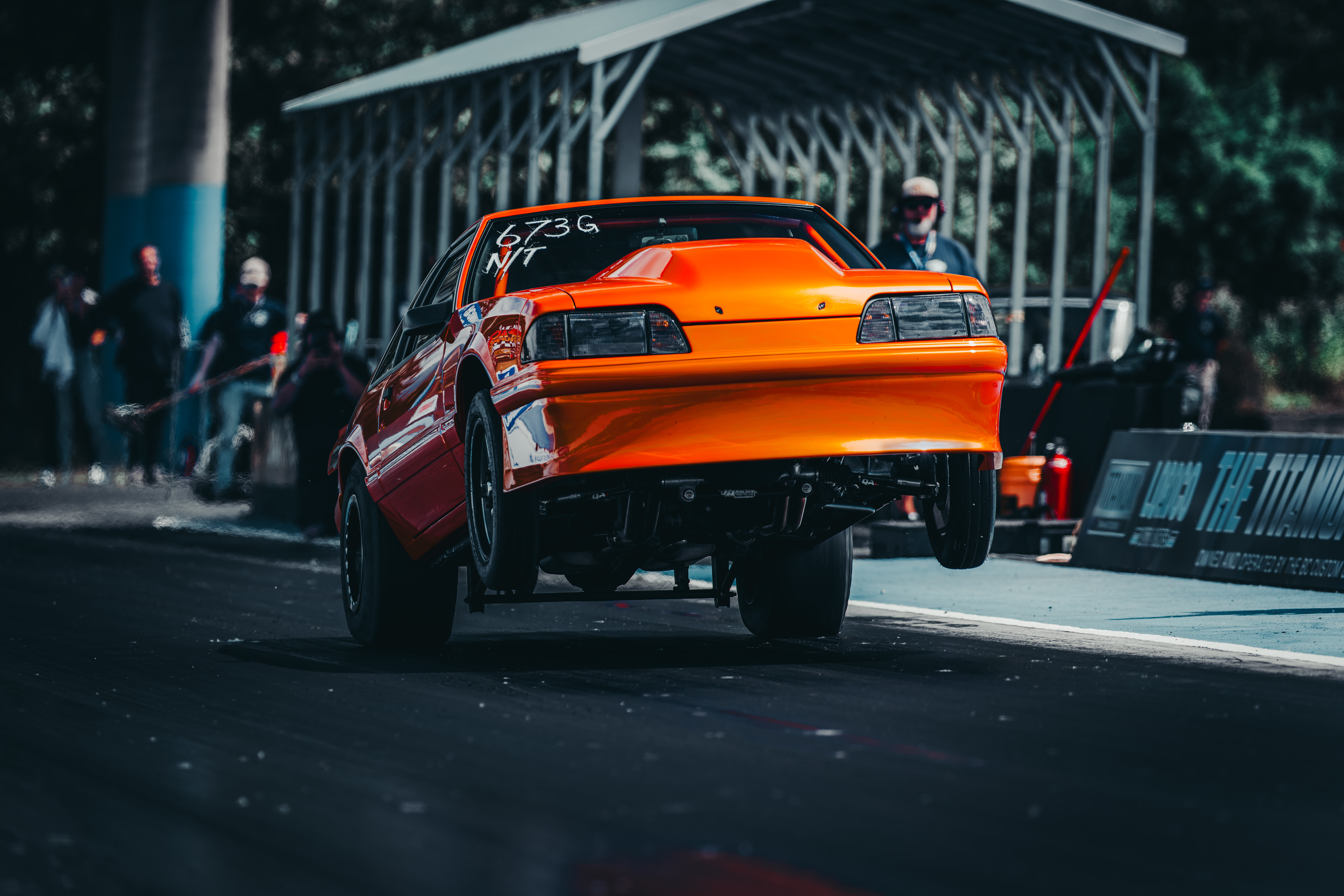 Orange drag racing car lifting front wheels off the track during a race start with Streetcar Addiction
