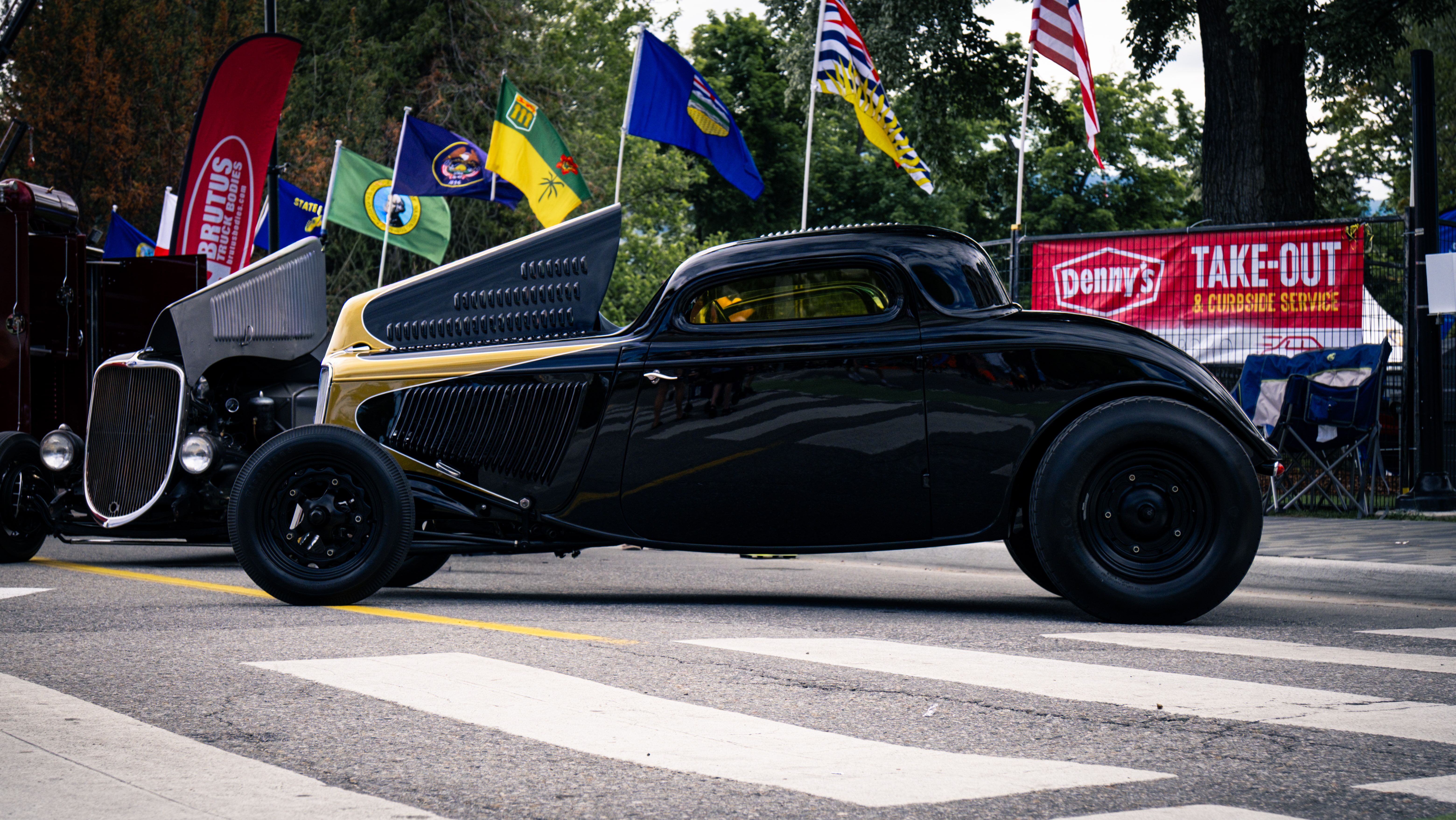 Red vintage Plymouth Superbird muscle car parked on asphalt with trees and buildings in the background with Streetcar Addiction