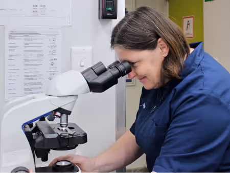 A woman in a blue lab coat looking through a microscope in a laboratory setting to show Citivets in-house lab