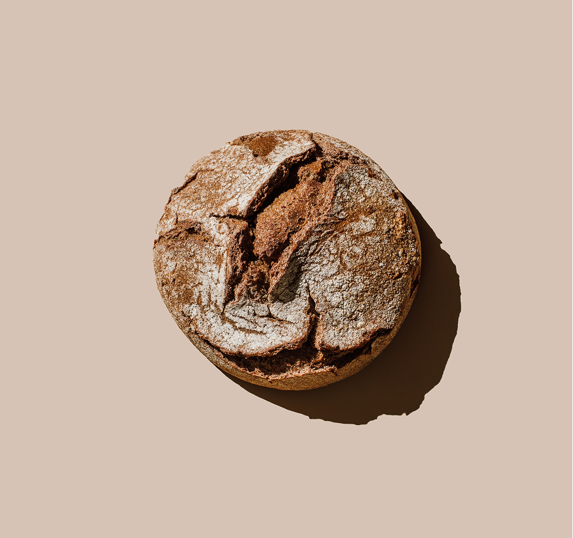 Rundes rustikales Brot mit bemehlter, aufgerissener Kruste auf beigem Hintergrund von oben