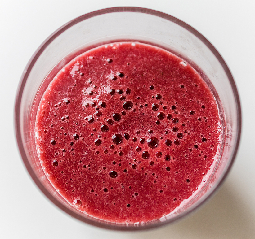 Glass of red berry smoothie seen from above on a white surface