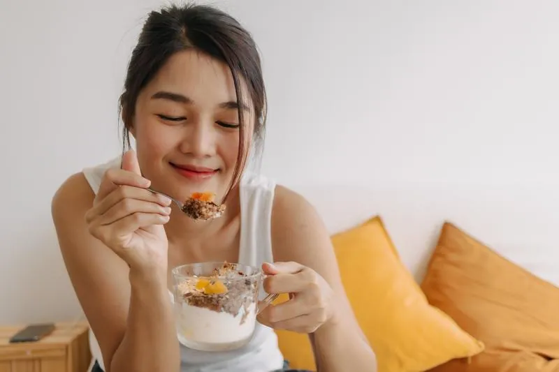 Junge Frau genießt Joghurt mit Fruchtzubereitung und Crunch-Topping – moderner Milchprodukte-Trend mit innovativen Fruchtlösungen von AGRANA.