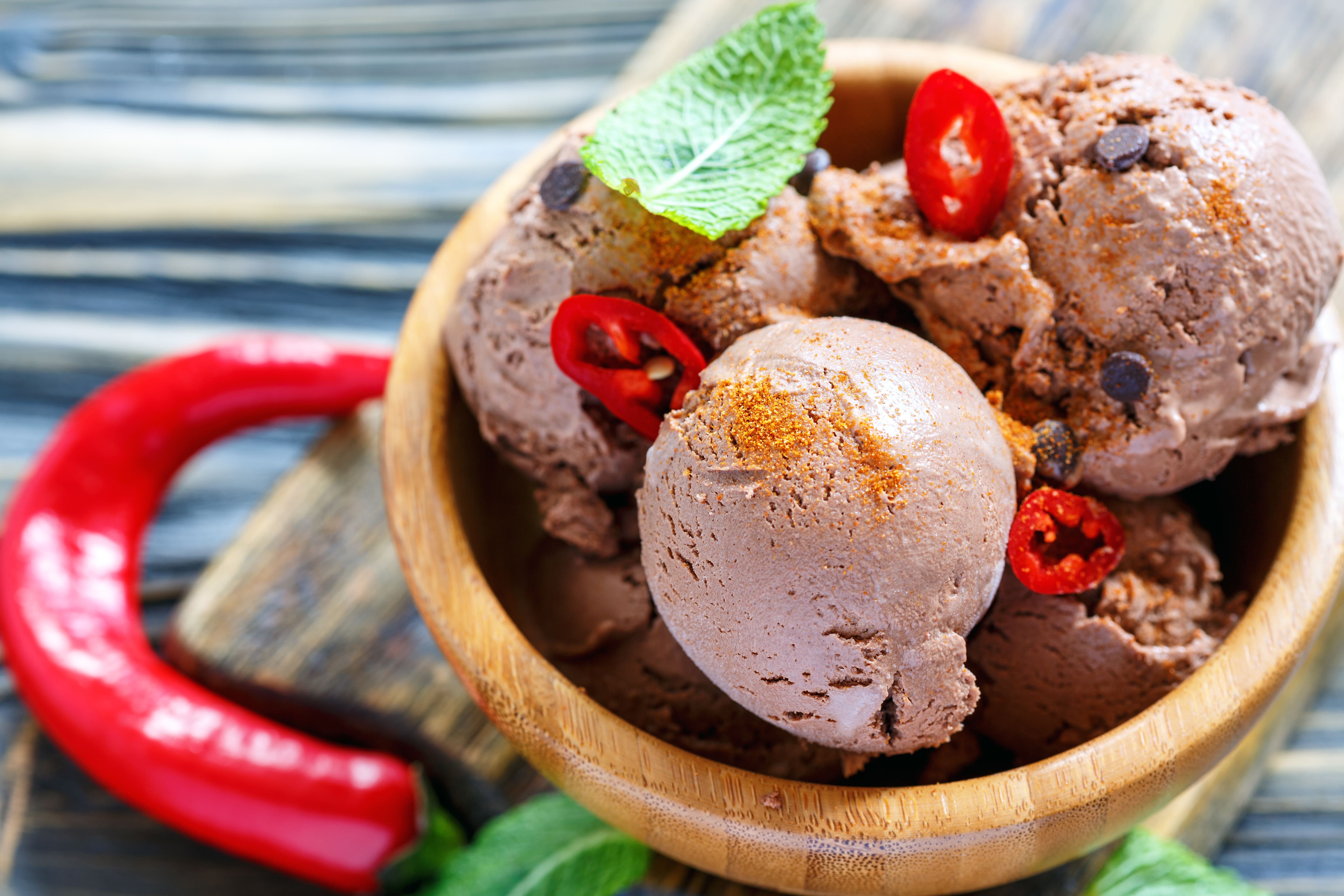 Bowl of chocolate ice cream scoops topped with fresh chili peppers, chocolate chips and mint