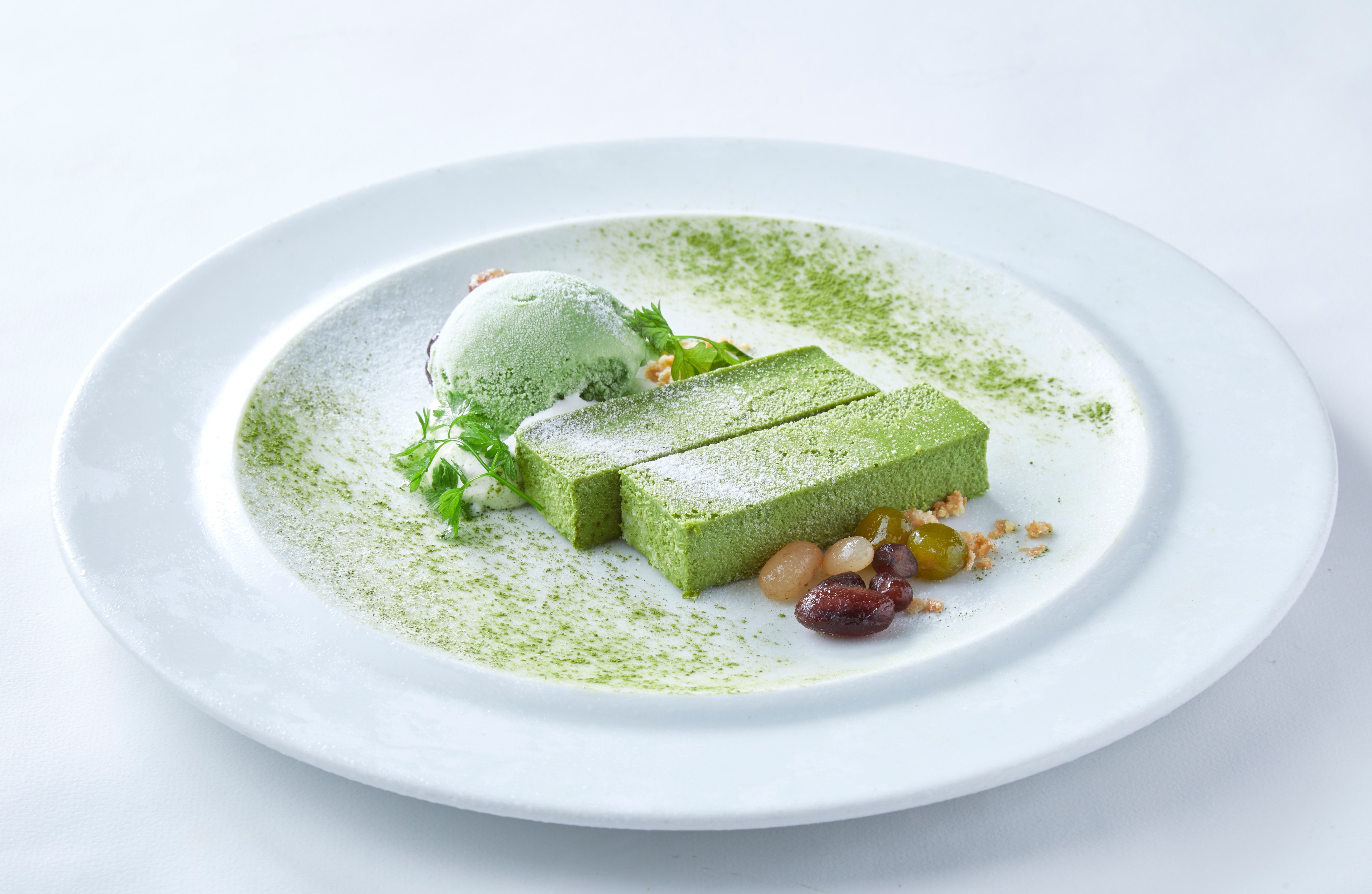 Matcha tiramisu dessert with a scoop of green tea ice cream, dusted with matcha powder on a white plate