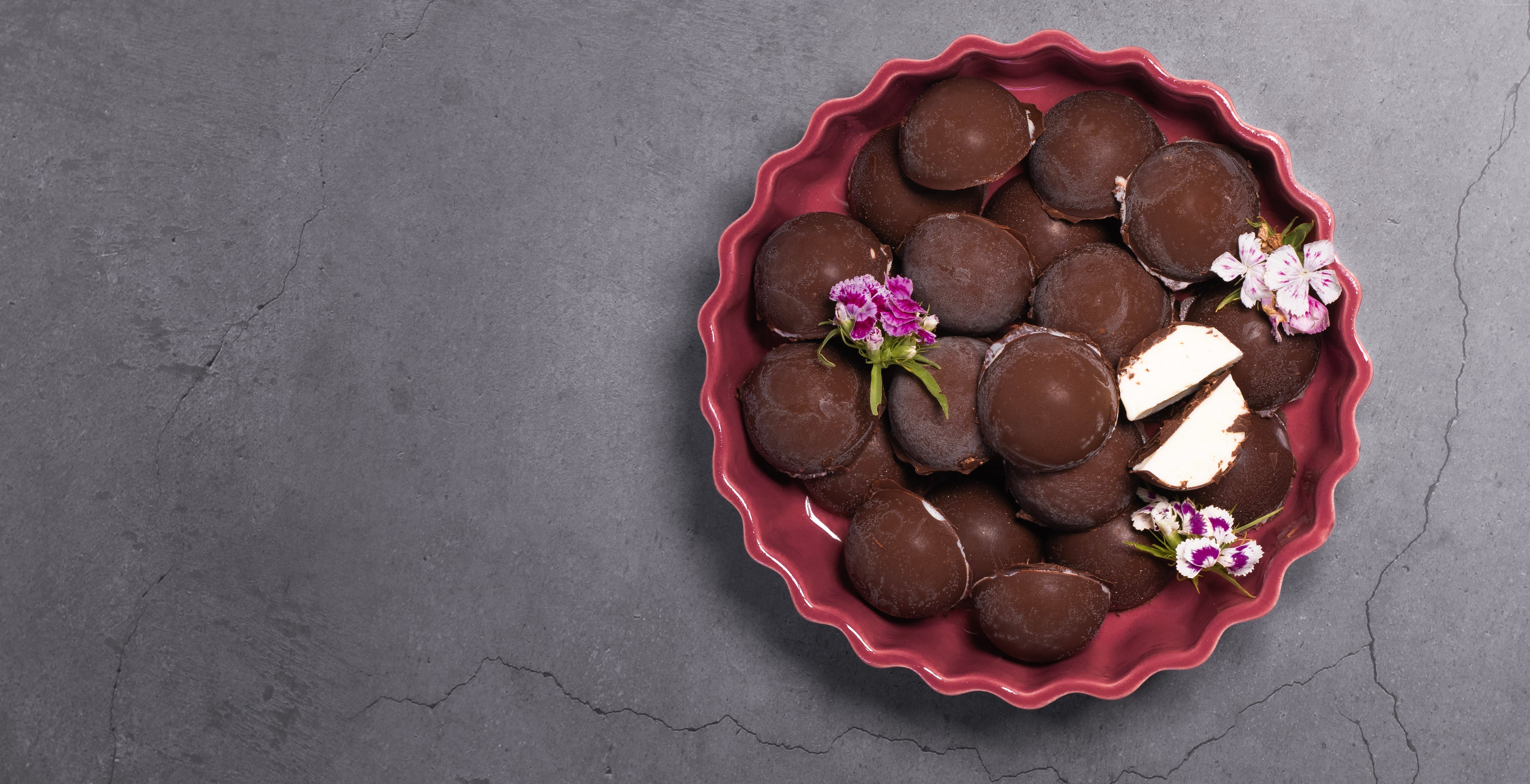 Chocolate-coated pastries with a cream filling arranged in a red dish with edible flowers