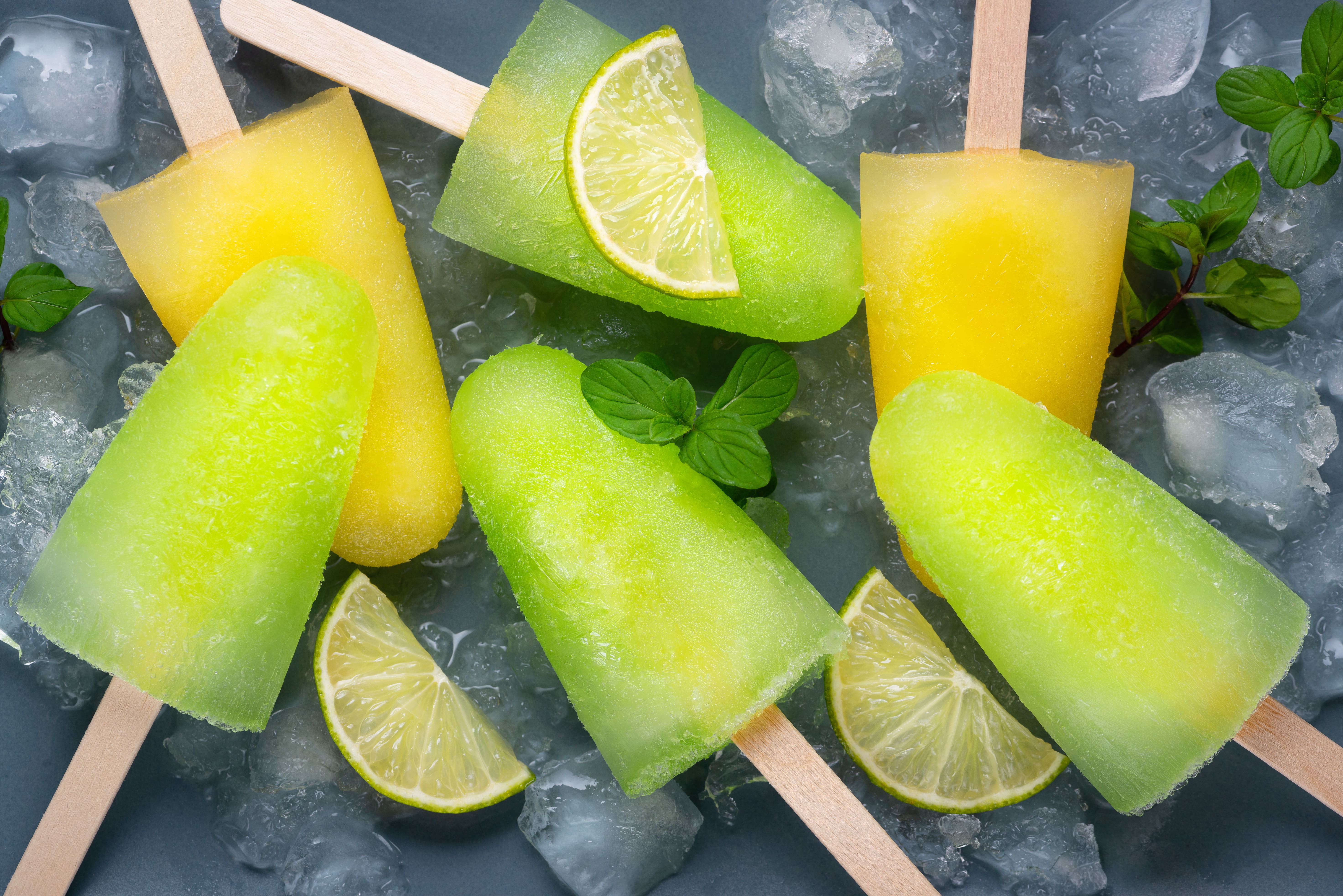 Mango and lime popsicles arranged on crushed ice with mint leaves and lime wedges