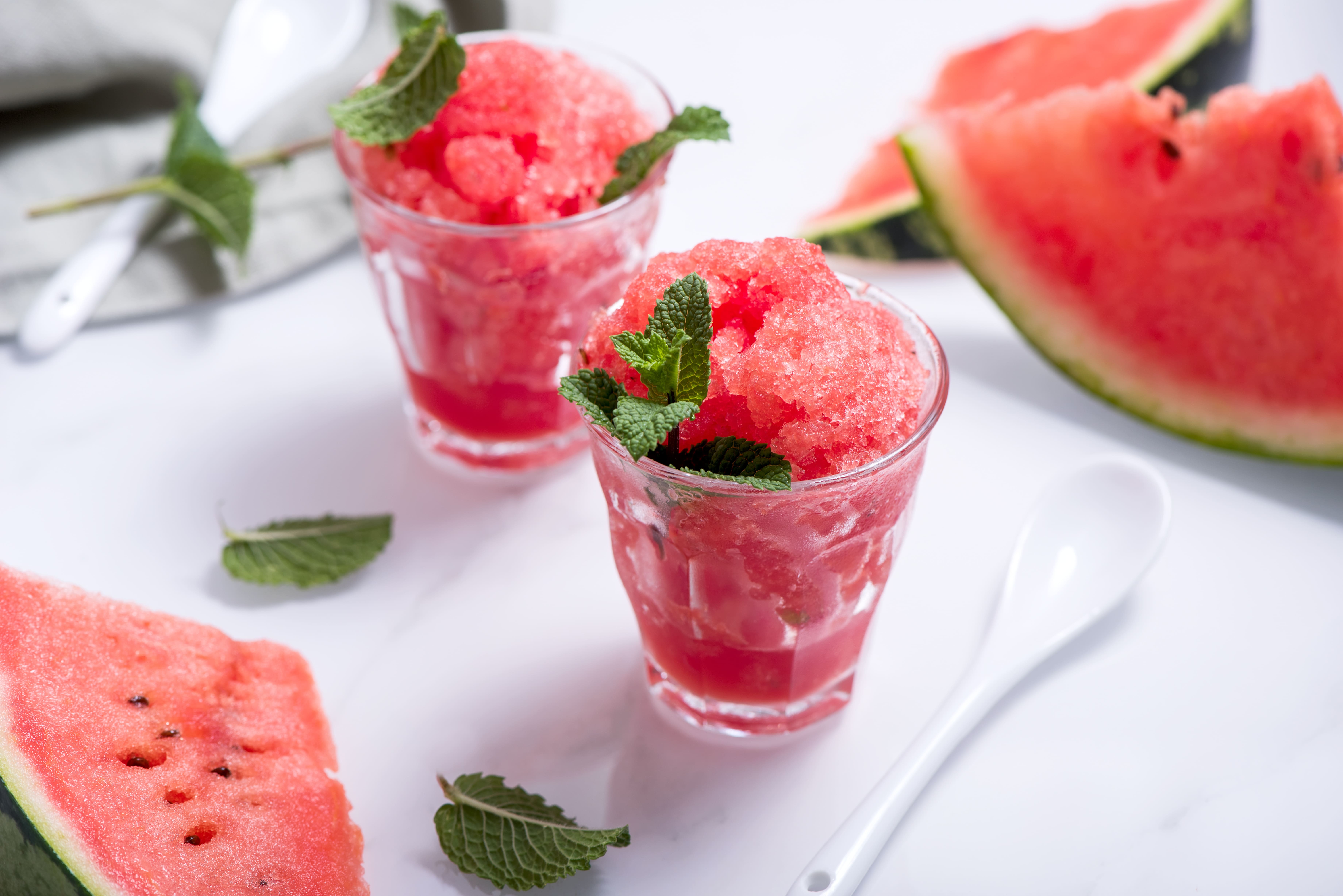 Two glasses of watermelon granita garnished with mint, next to watermelon slices