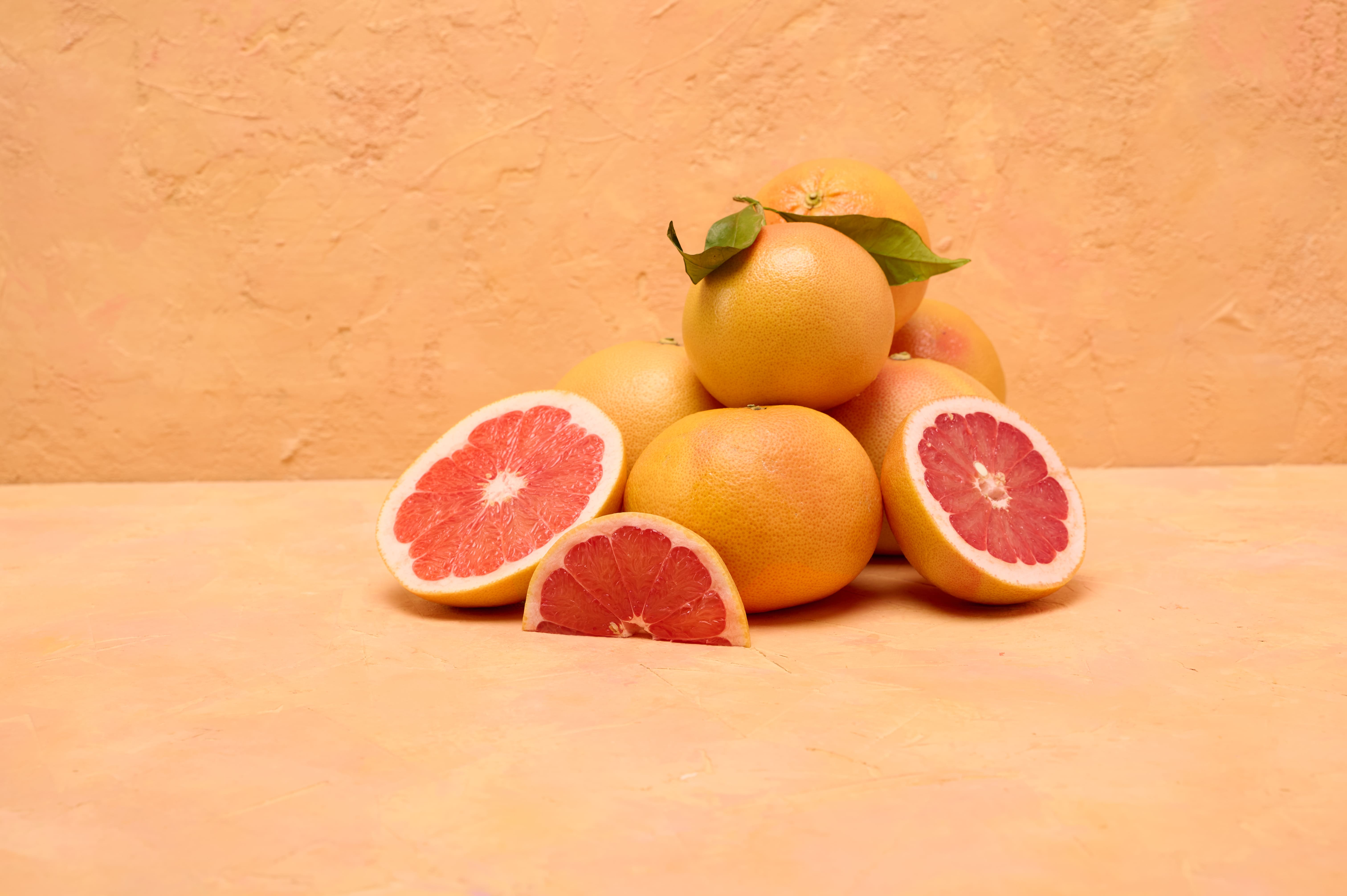 Ganze und halbierte Grapefruits auf warmem Hintergrund, die ihr leuchtend pinkes Fruchtfleisch zeigen.