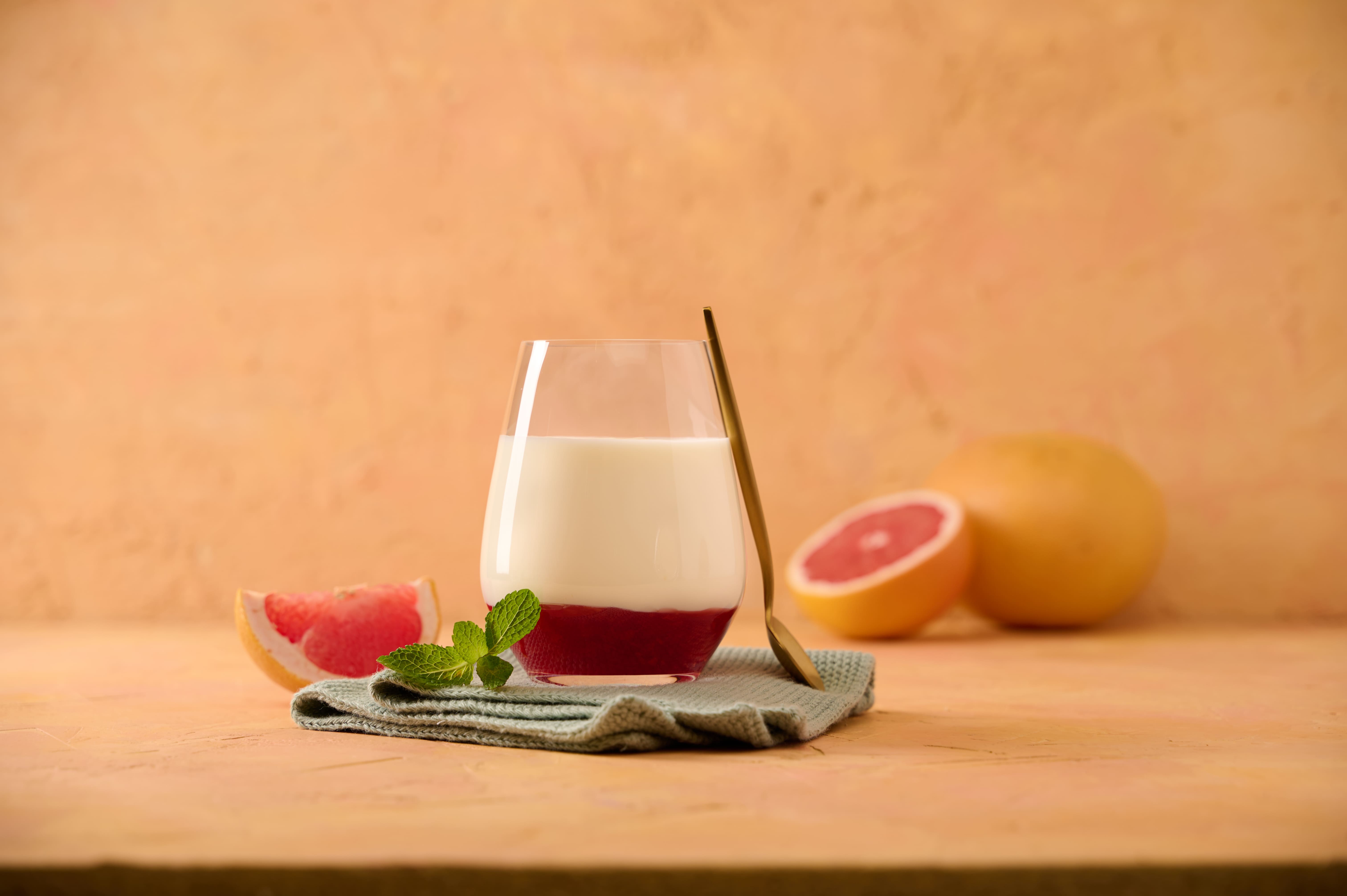 Glass of yogurt layered with red grapefruit sauce, garnished with mint next to grapefruit halves
