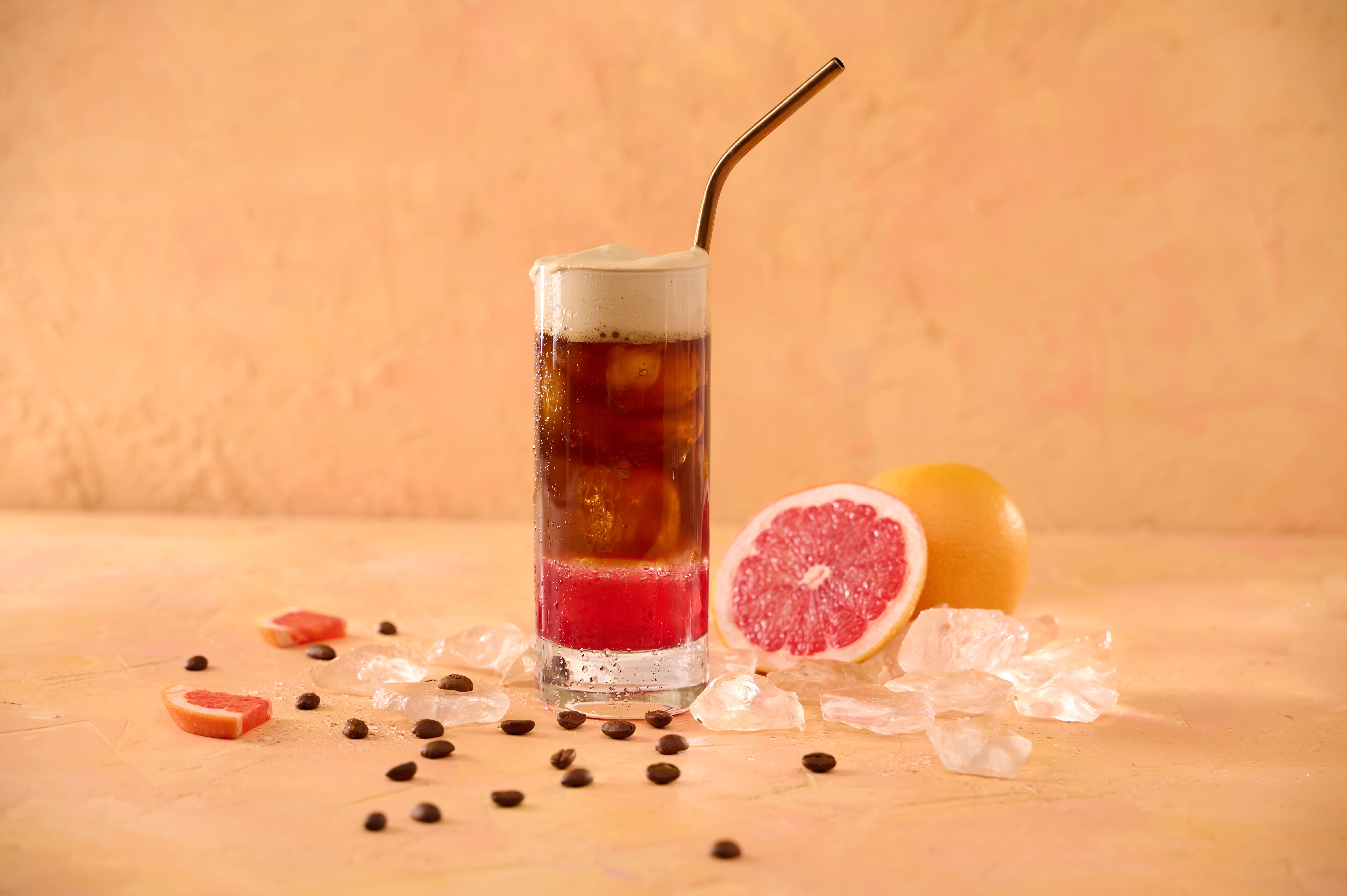 Tall glass of grapefruit cold brew coffee with ice and coffee beans next to grapefruit halves