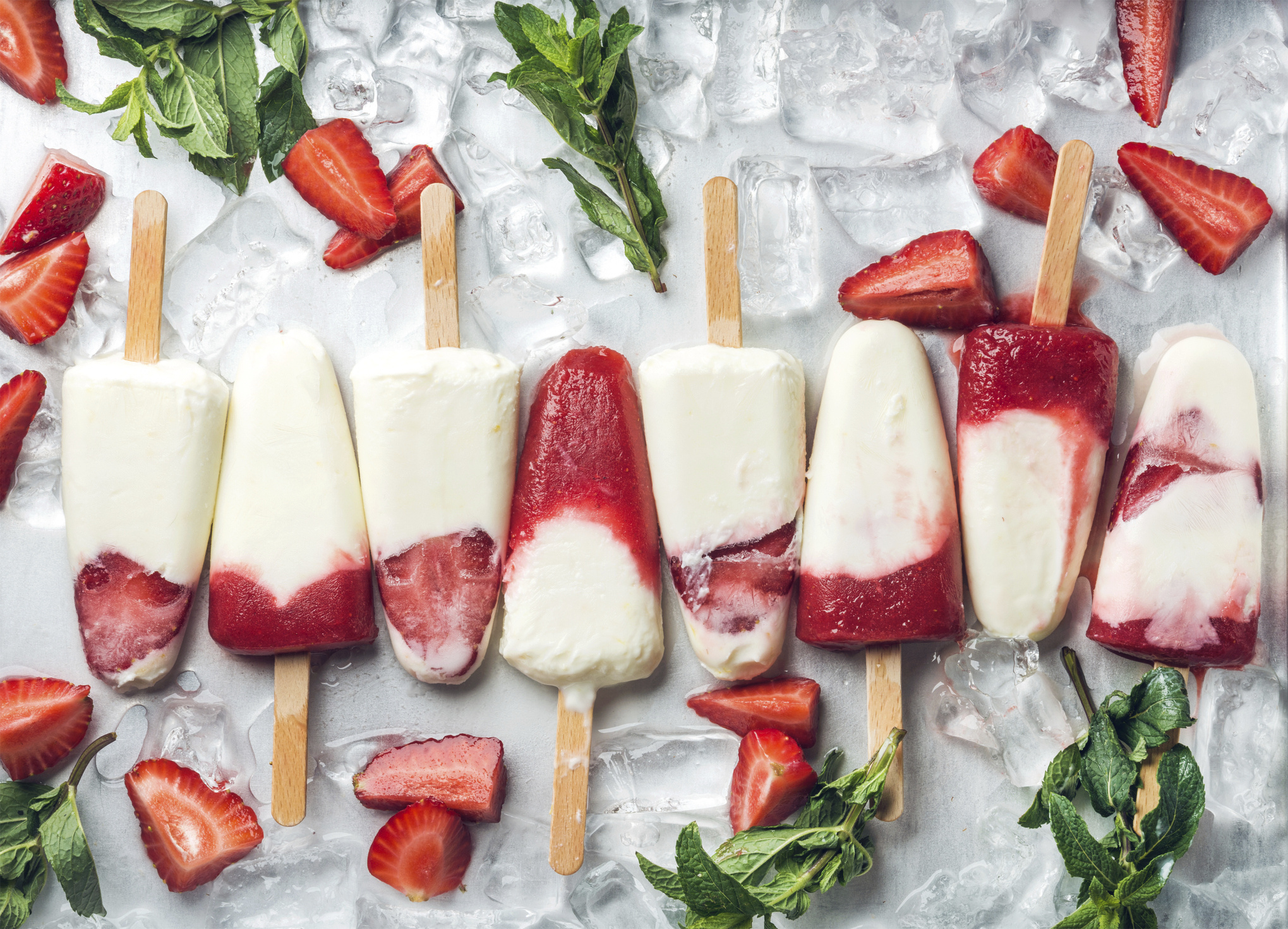 Row of white and red layered ice pops with strawberry pieces, mint leaves and ice cubes