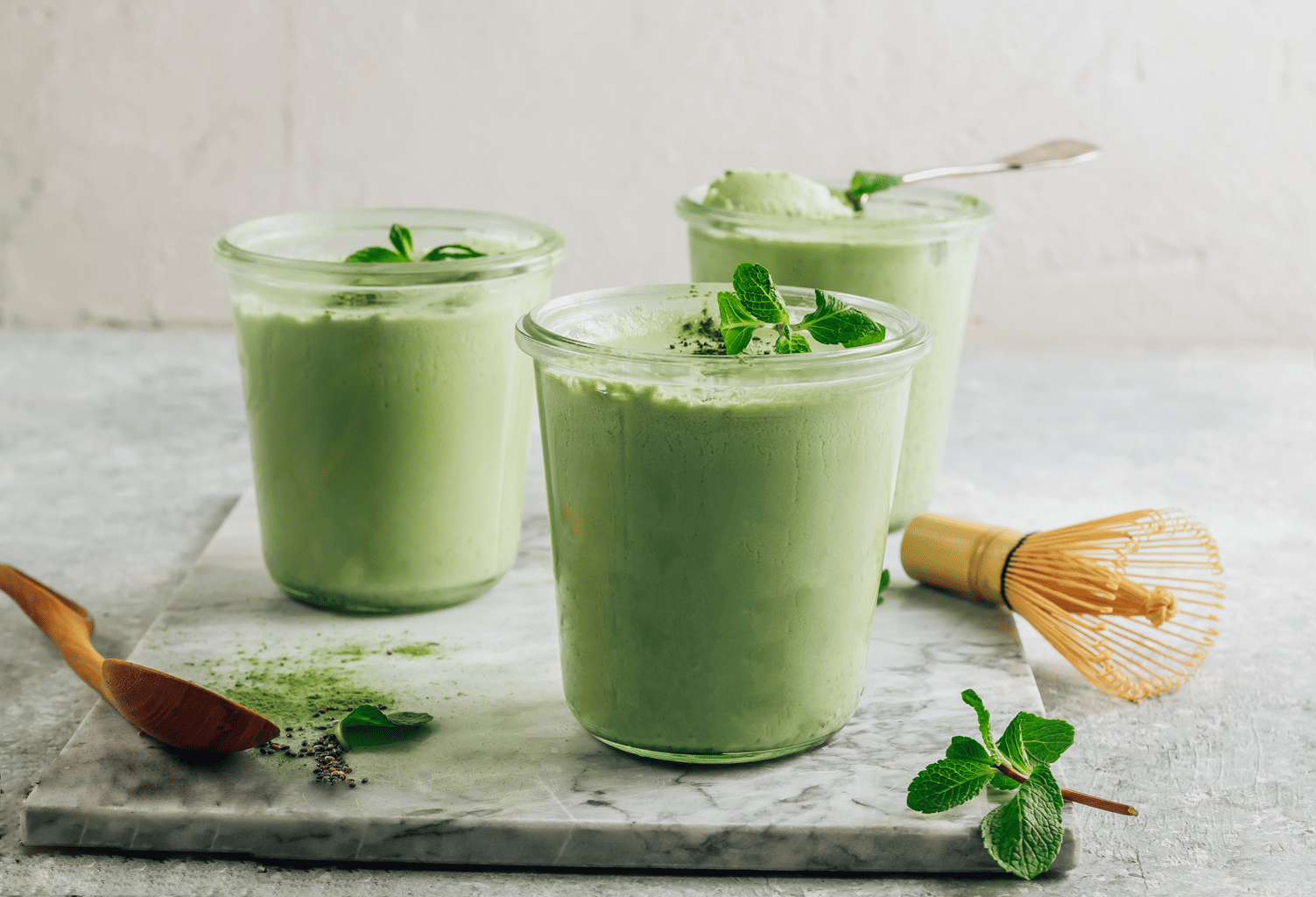 Drei Becher mit cremigem grünem Matcha-Dessert oder Smoothie, garniert mit frischer Minze. [AI generated]