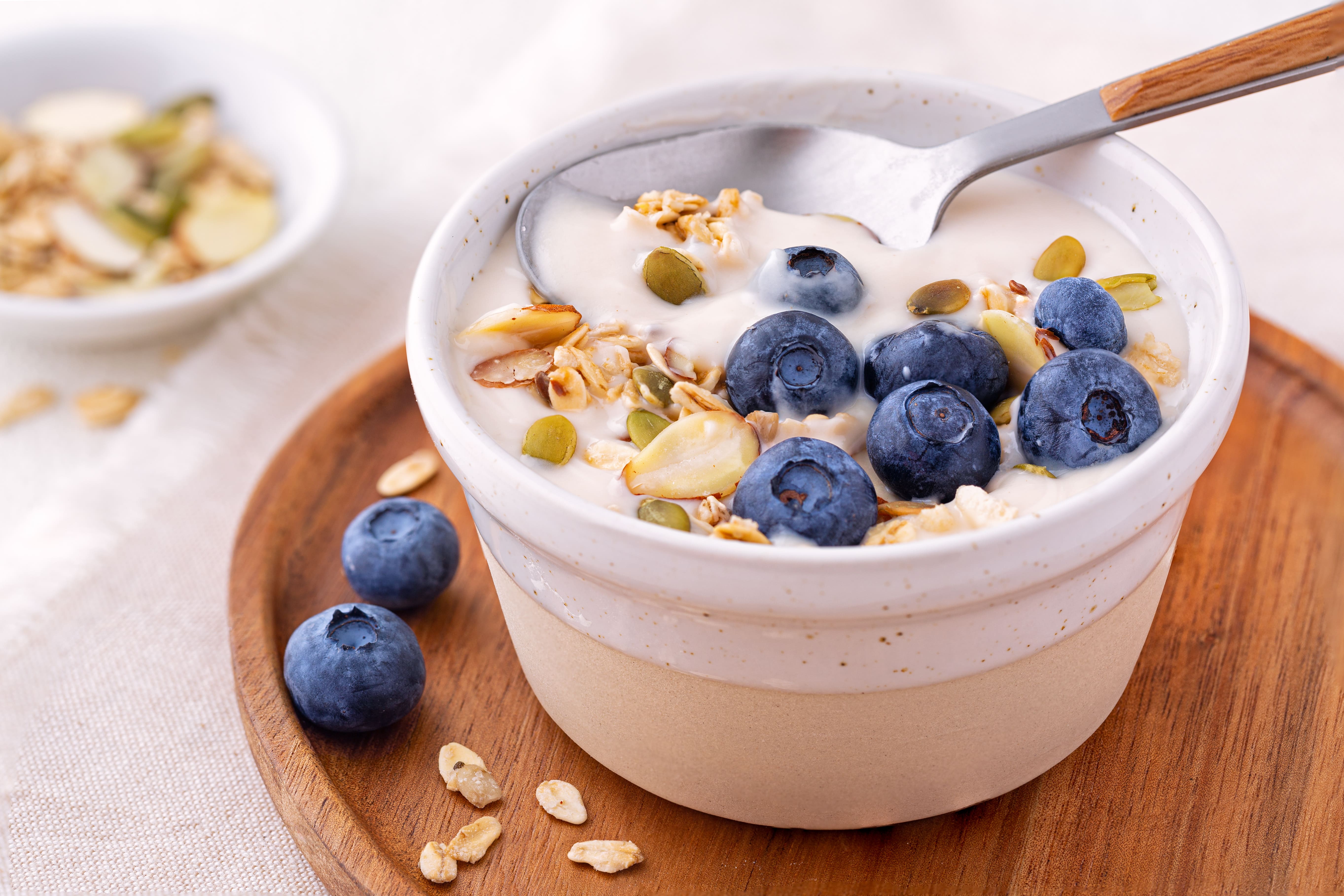 Bowl of yogurt topped with granola, blueberries and pumpkin seeds on a wooden plate
