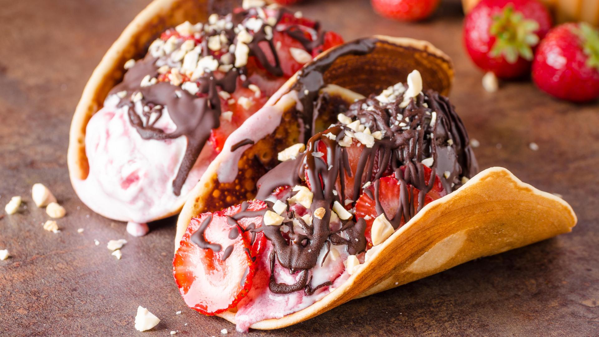 Dessert taco shells filled with cream, strawberries and chocolate drizzle, topped with chopped nuts