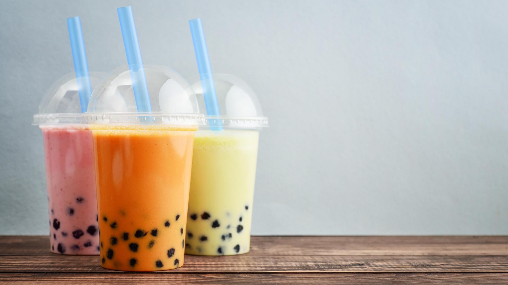 Three plastic cups of colourful bubble tea with tapioca pearls and straws on a wooden table