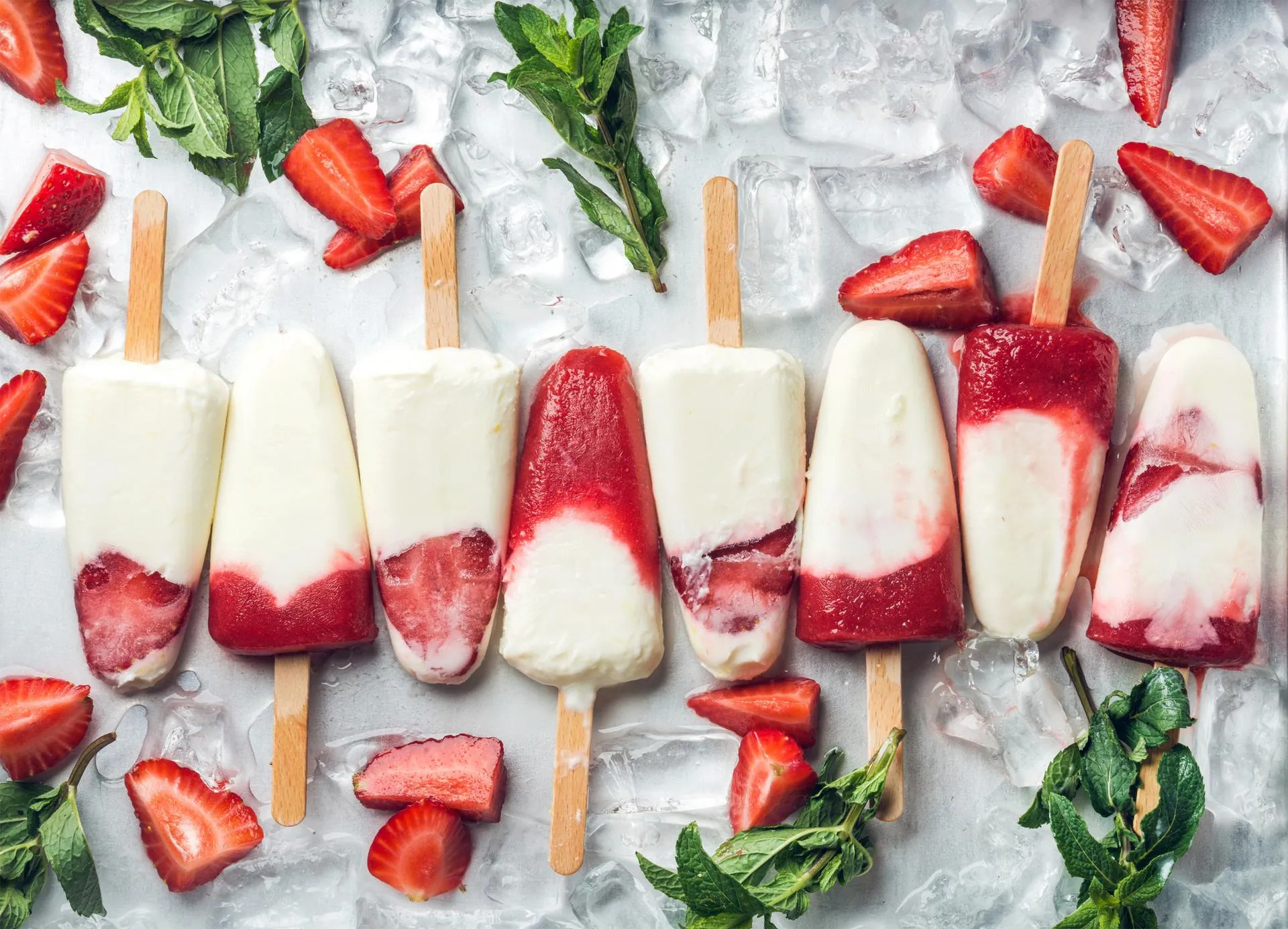 Erdbeer-Joghurt-Eis am Stiel auf Eis angerichtet mit frischen Erdbeeren und Minze