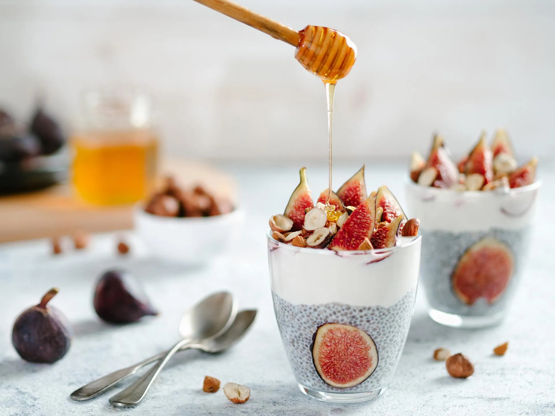 Geschichtetes Joghurt-Dessert mit Chiasamen, frischen Feigen und Haselnüssen, beträufelt mit Honig