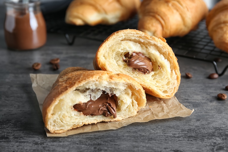 Halbiertes Croissant mit Schokoladen-Haselnuss-Creme-Füllung, weitere Croissants auf einem Gitter dahinter