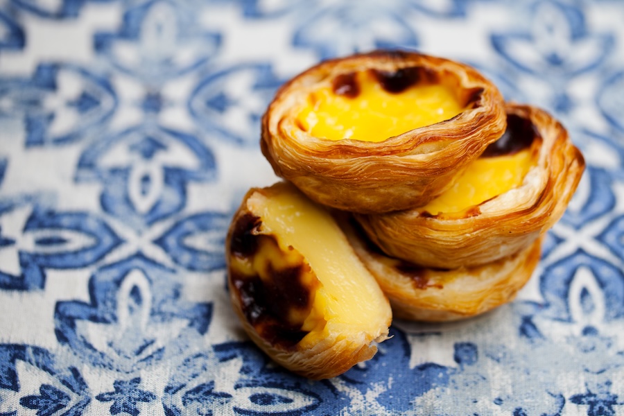 Drei portugiesische Pudding-Tartelettes mit karamellisierter Oberfläche auf blau-weiß gemustertem Tuch