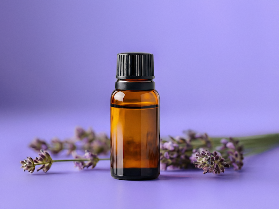 Kleines braunes Glasfläschchen mit Aromakonzentrat und Lavendelzweigen vor violettem Hintergrund