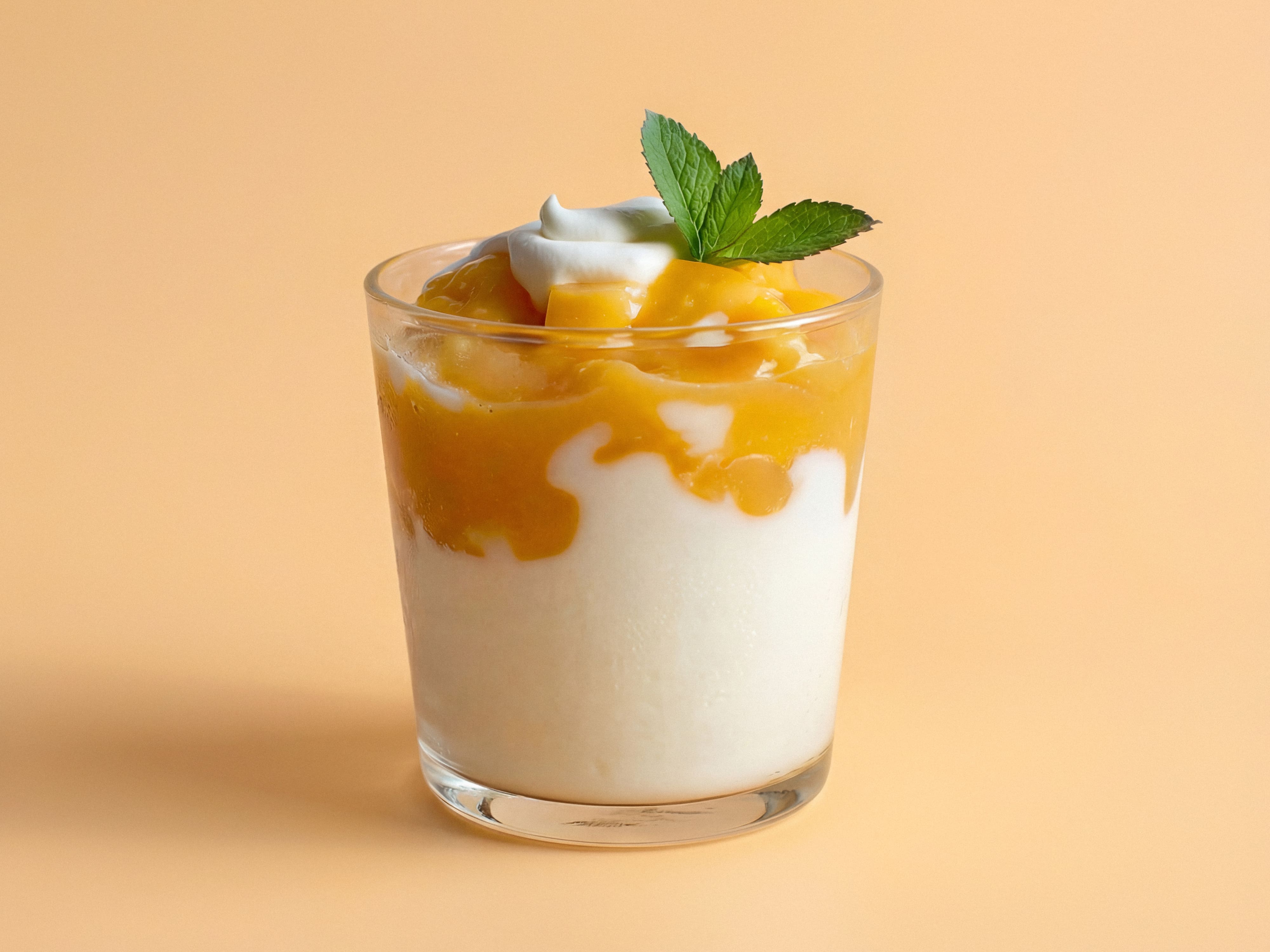 Glas Joghurt mit Mango-Fruchtschicht obenauf, garniert mit Minze und einem Klecks Sahne