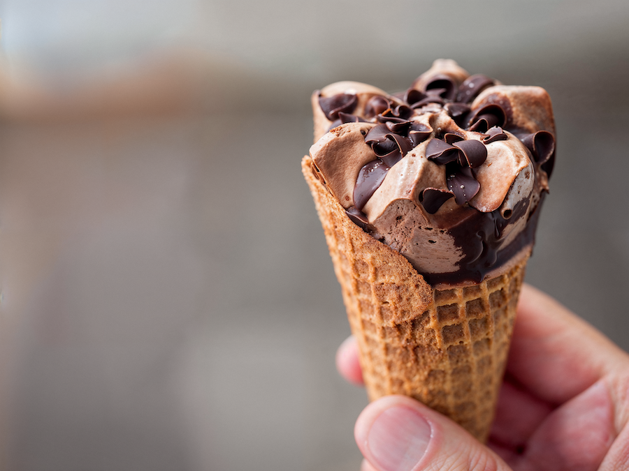 Hand hält eine Waffeltüte mit Schokoladeneis, Schokoladen-Swirl und Schokoladenstückchen