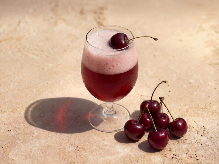 Glas mit schaumigem Kirschgetränk und frischen Kirschen auf sonnigem Steinuntergrund