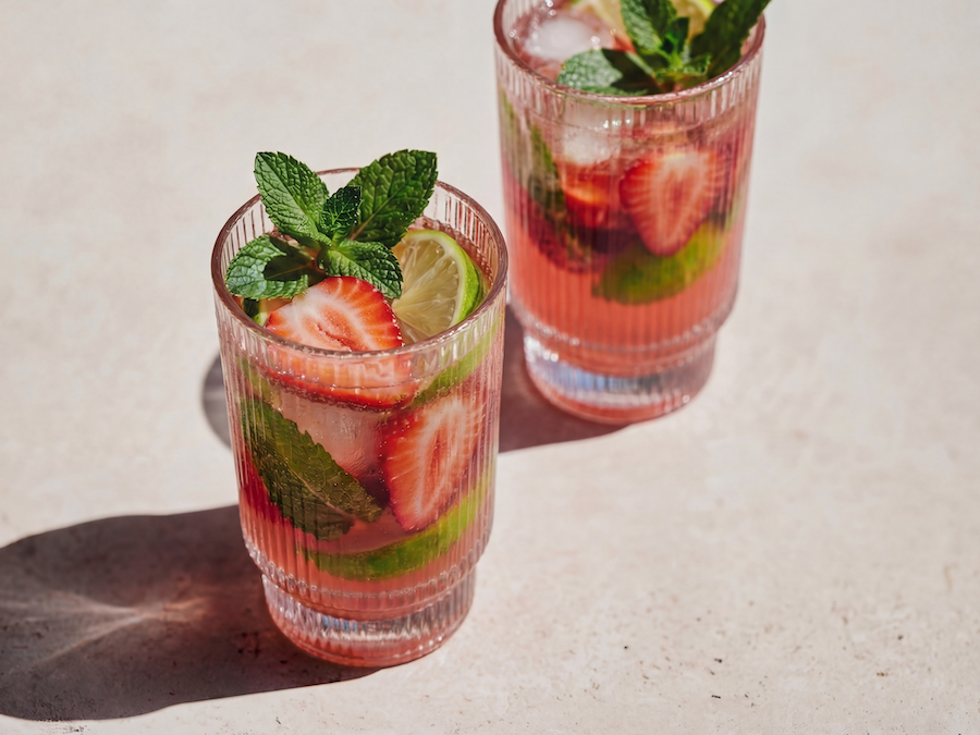 Zwei geriffelte Gläser Erdbeergetränk mit Minze, Limette und Eis auf sonnigem Steinuntergrund