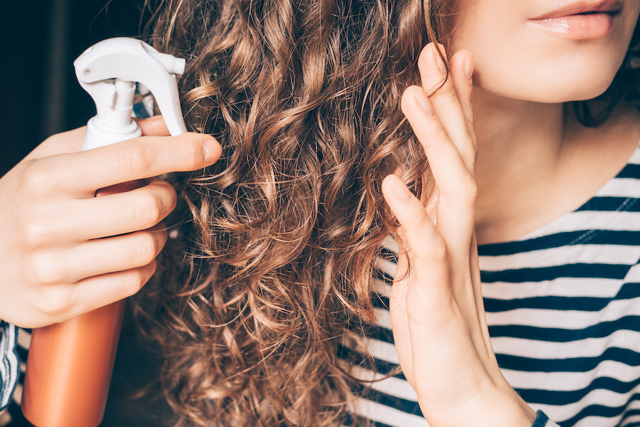 Frau sprüht Stylingprodukt in ihr langes lockiges Haar