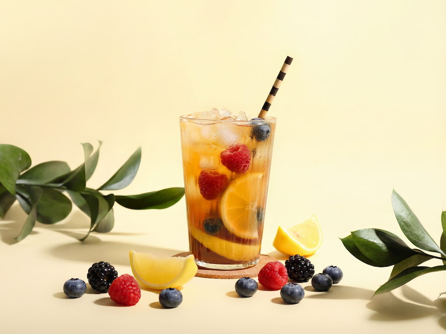Eisgekühlte Fruchtlimonade mit Orangenscheiben, Himbeeren und Heidelbeeren und gestreiftem Strohhalm