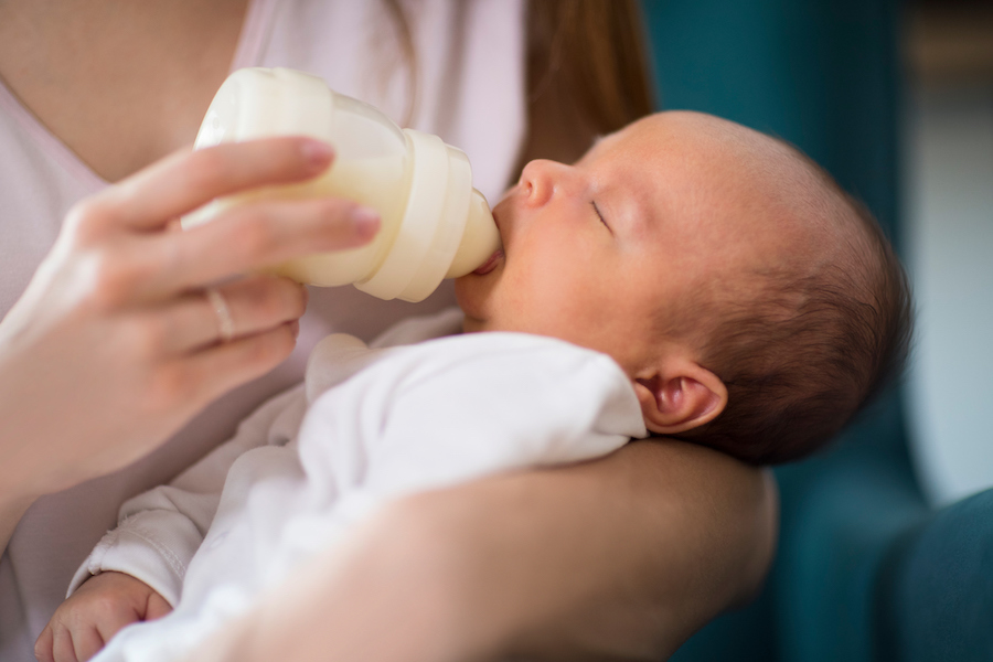 Mutter füttert ein schlafendes Neugeborenes mit einer Flasche Säuglingsnahrung