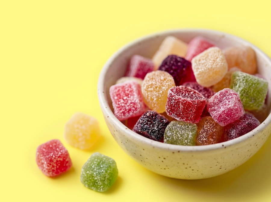 Schale mit bunten, gezuckerten Fruchtgummi-Würfeln vor gelbem Hintergrund