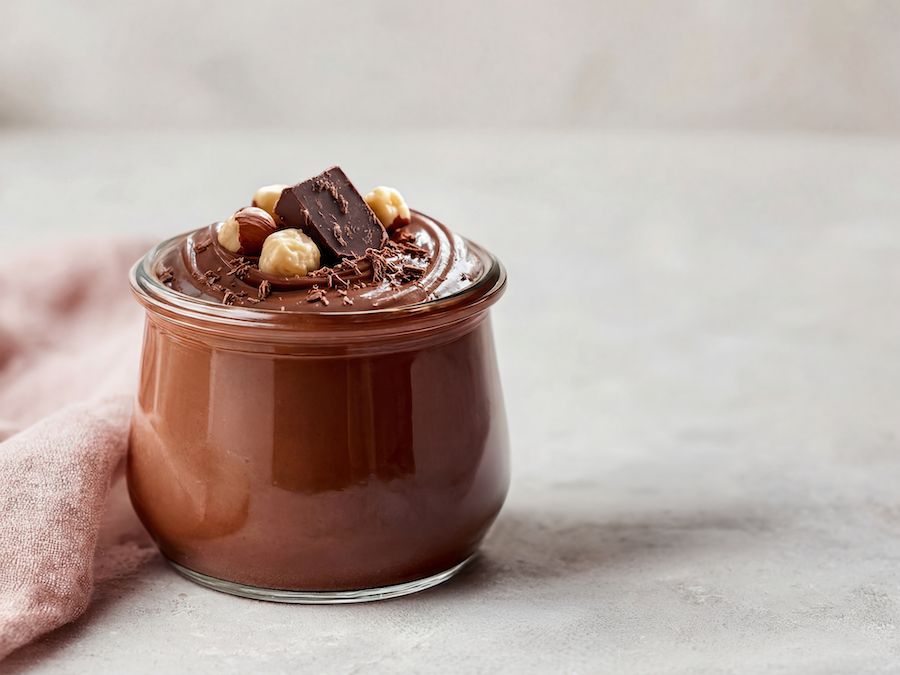 Glas mit Nuss-Nougat-Creme, garniert mit Haselnüssen und einem Stück dunkler Schokolade