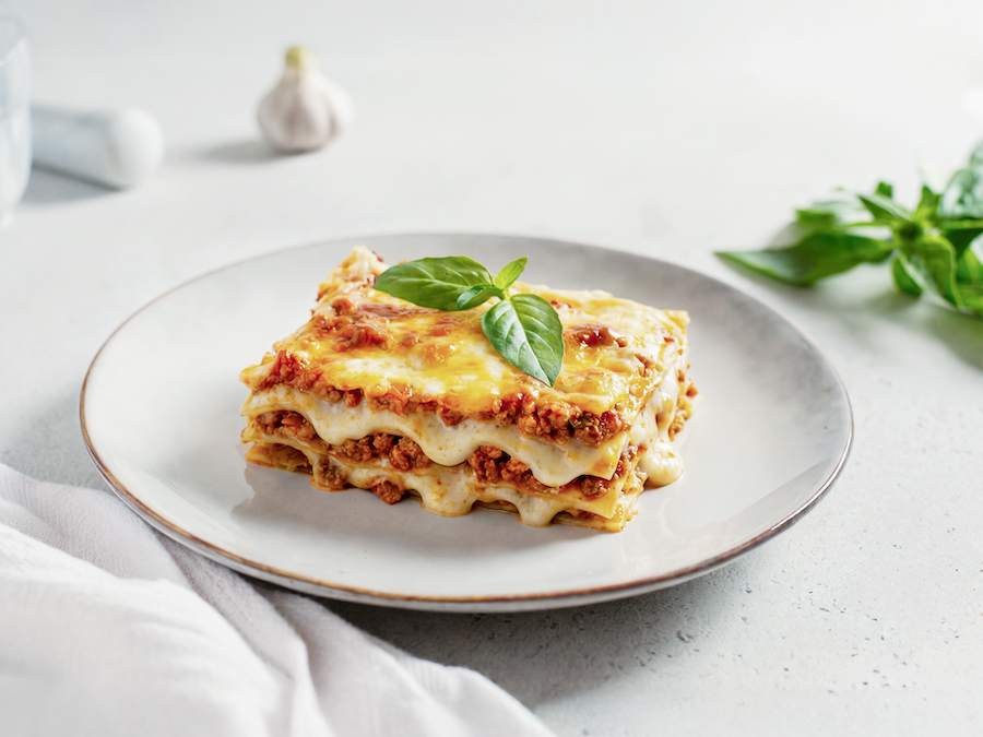 Stück Lasagne mit Fleischsauce und geschmolzenem Käse, mit Basilikum garniert auf weißem Teller