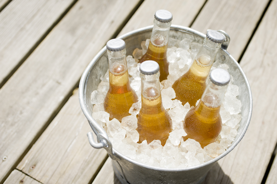 Fünf Flaschen Biermischgetränk in einem Metalleimer voller Eis auf einer Holzterrasse