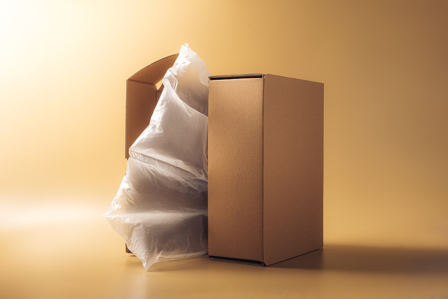 Brauner Karton mit transparenten Luftpolster-Verpackungskissen daneben vor beigem Hintergrund